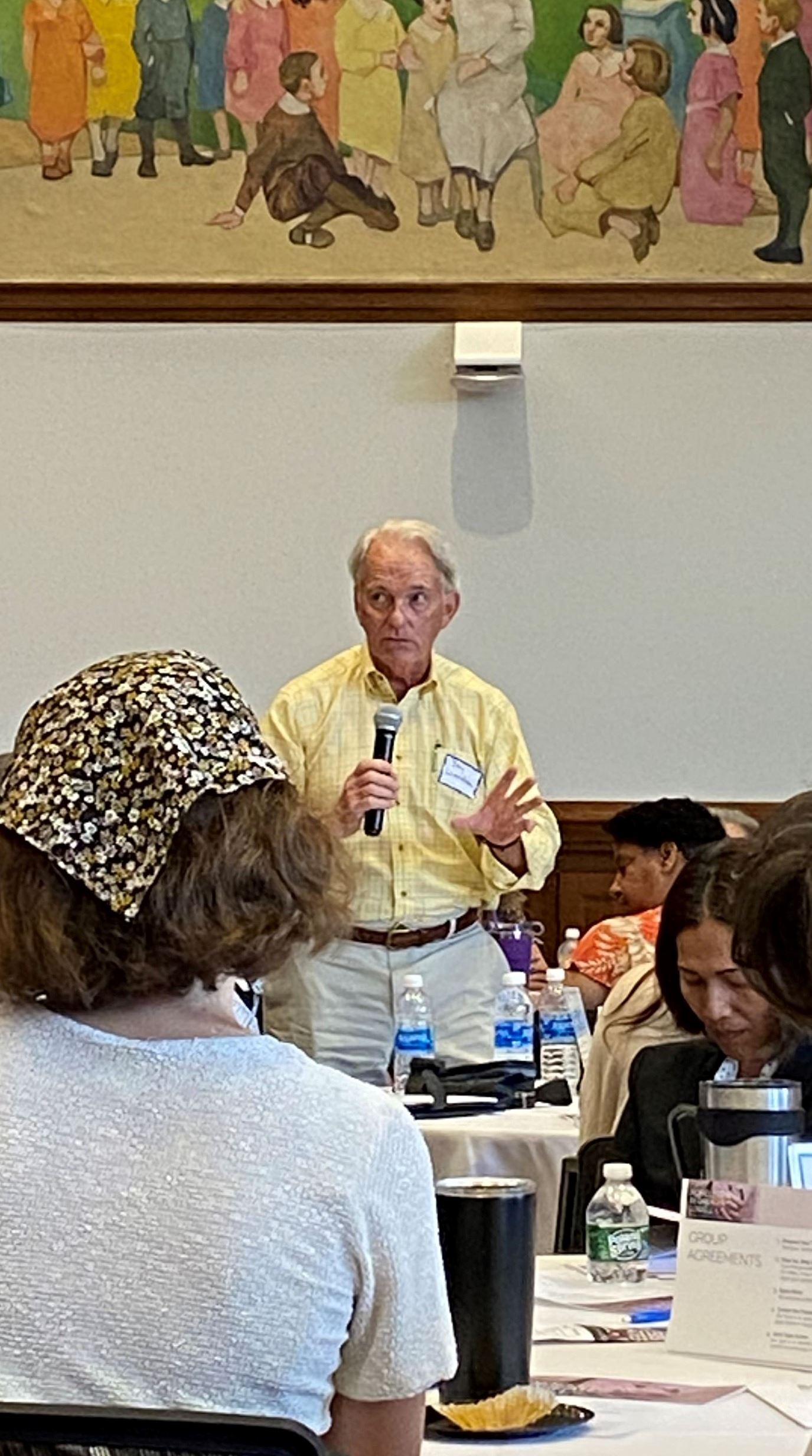 A man speaking with a microphone in front of people seated at a table